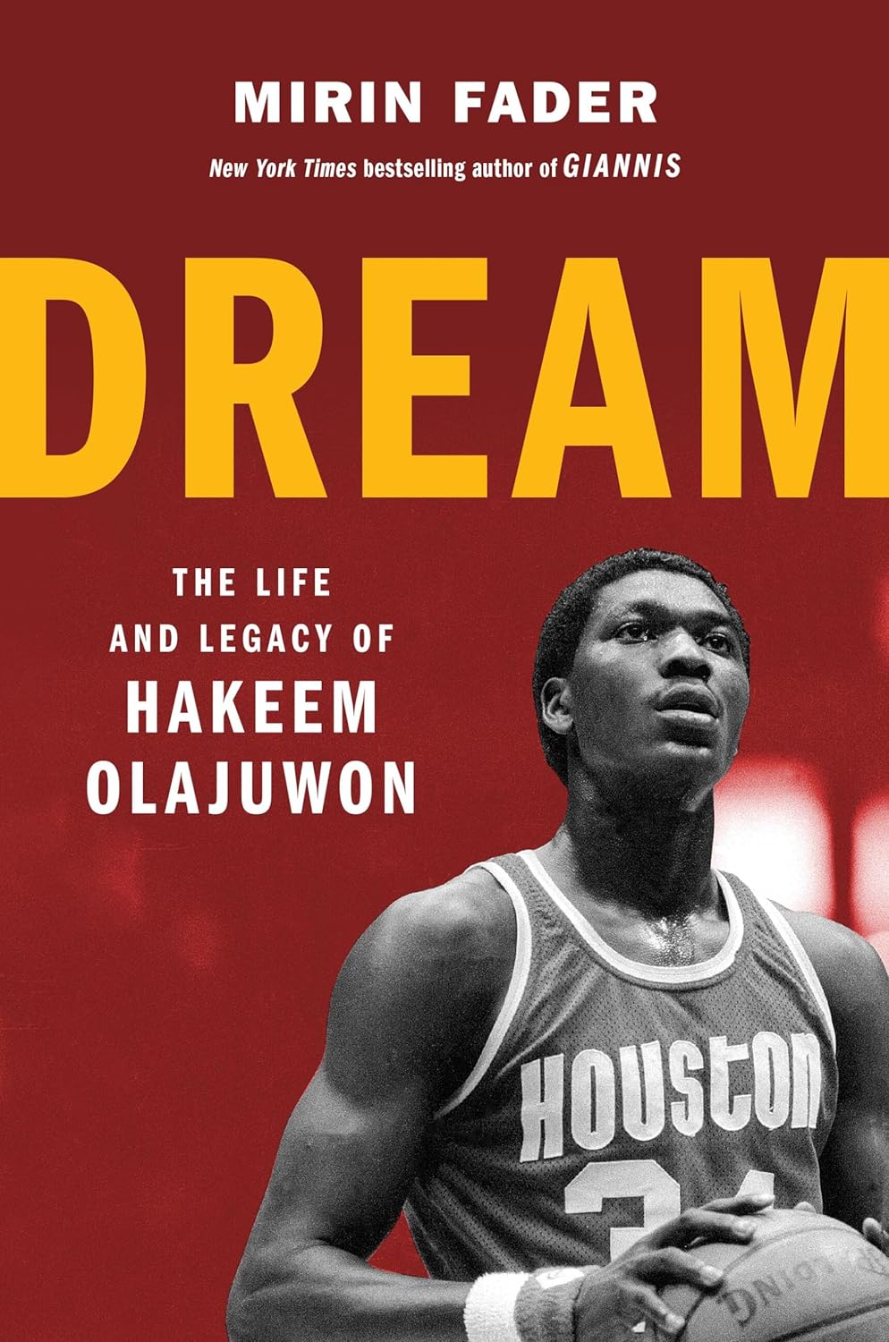 Book cover of 'Dream: The Life and Legacy of Hakeem Olajuwon' featuring a photo of Hakeem Olajuwon in a Houston Rockets basketball uniform, with the title in yellow and red text.