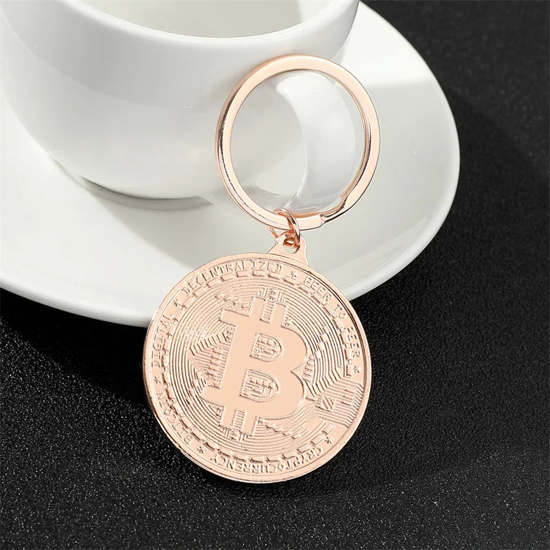 Rose gold Bitcoin keychain on a black surface with a white cup and saucer in the background.