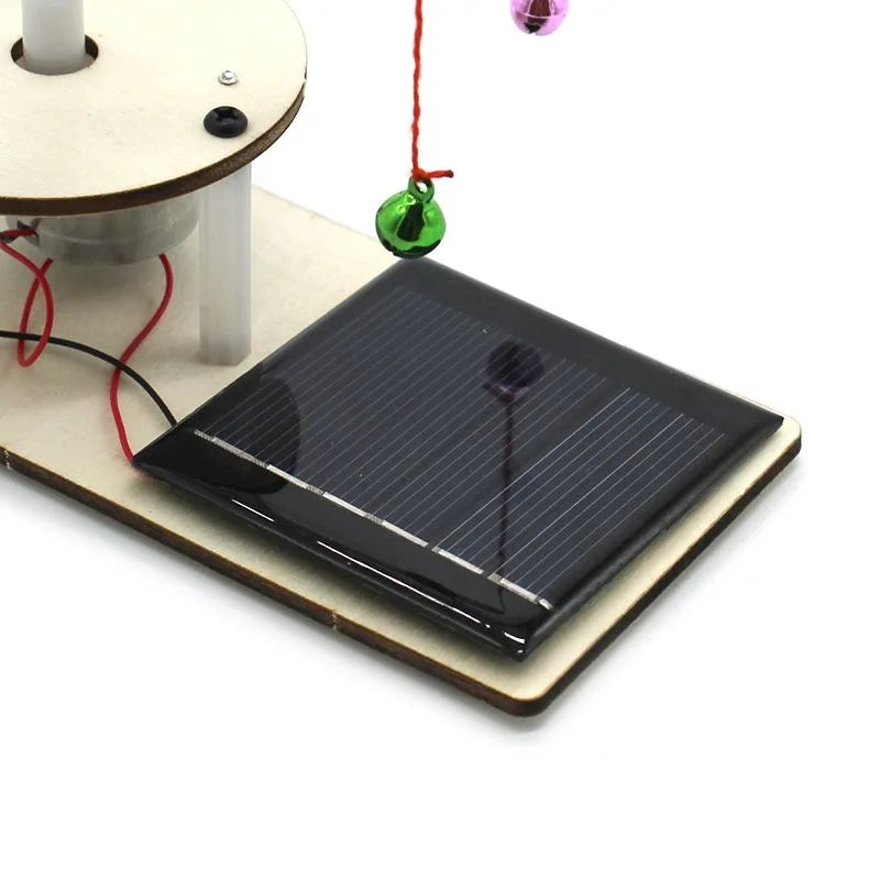 Small solar panel on a wooden base with wires and a bell on a white background