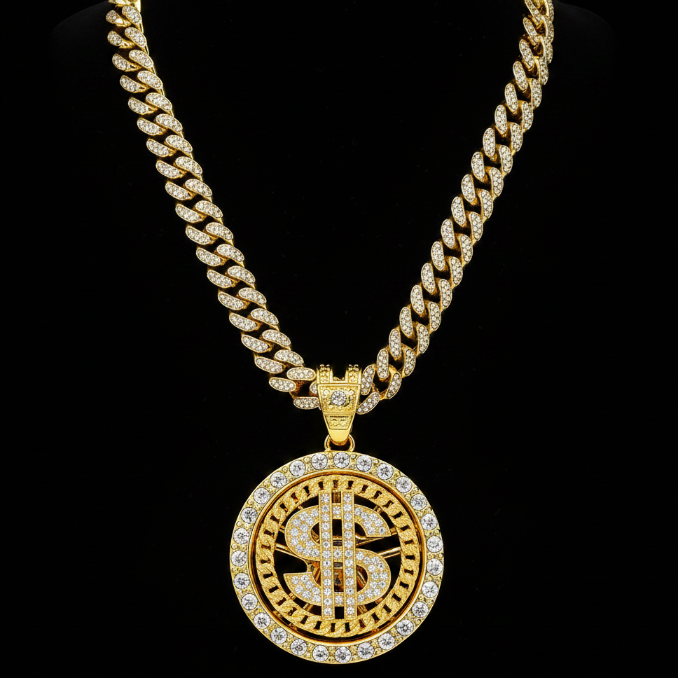 A gold-toned Cuban link chain necklace with a large circular pendant featuring a dollar sign motif, both heavily embellished with clear rhinestones, displayed against a solid black background.