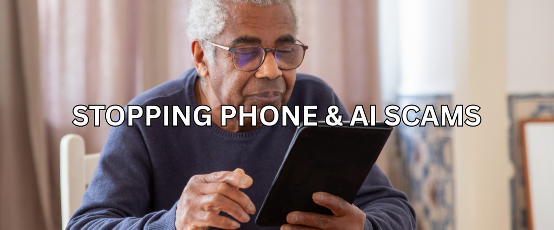 An older man with gray hair and glasses sits at a wooden table, holding a black tablet device and looking at its screen in a home setting.