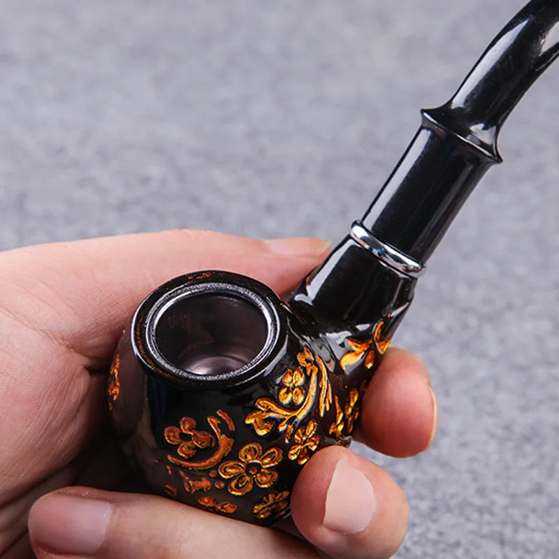 Hand holding a black and gold decorative pipe against a gray background