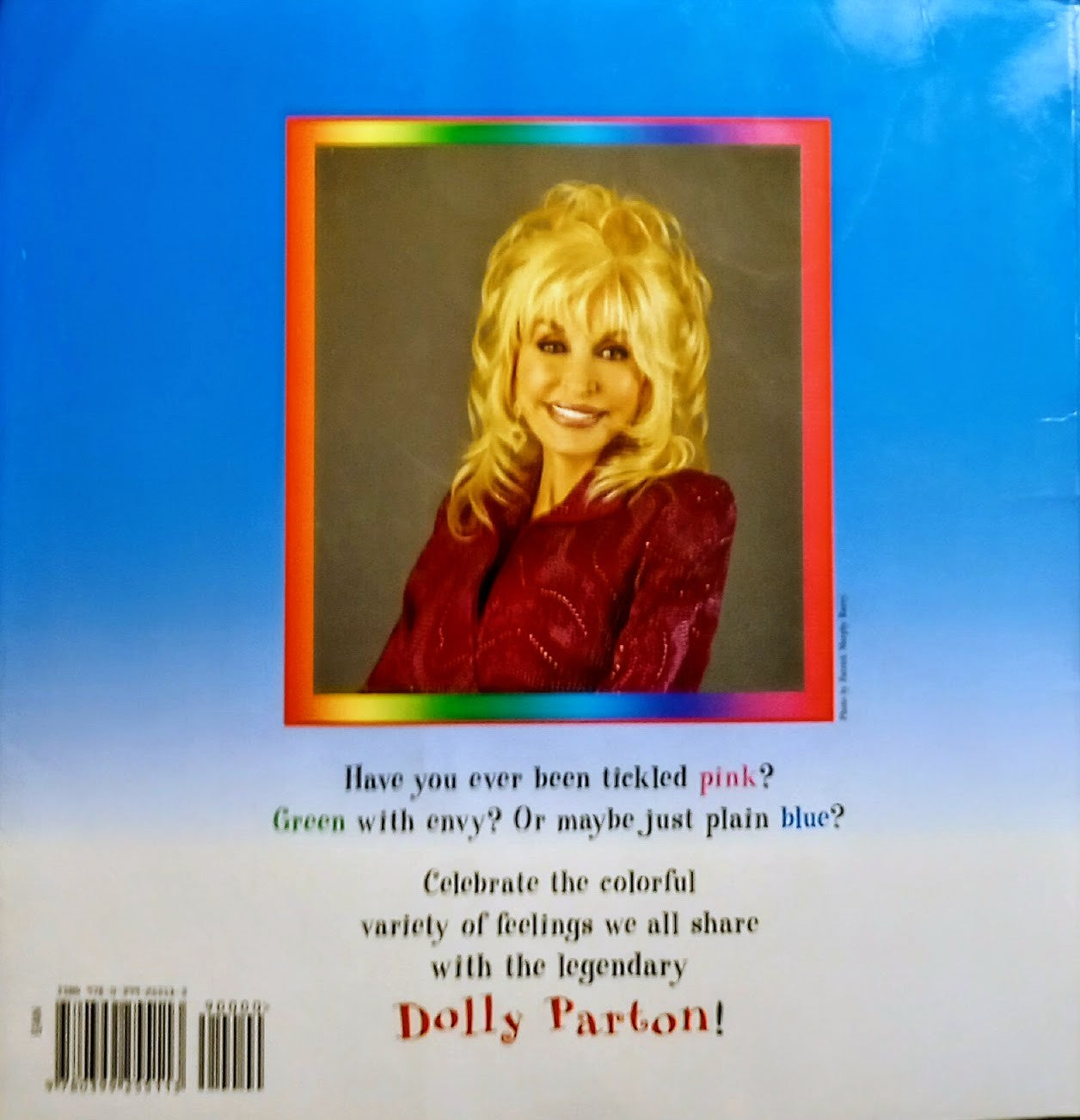 Back cover of a Dolly Parton printed item, featuring a portrait of Dolly in a red outfit with a rainbow border on a blue background, with text below and a barcode.