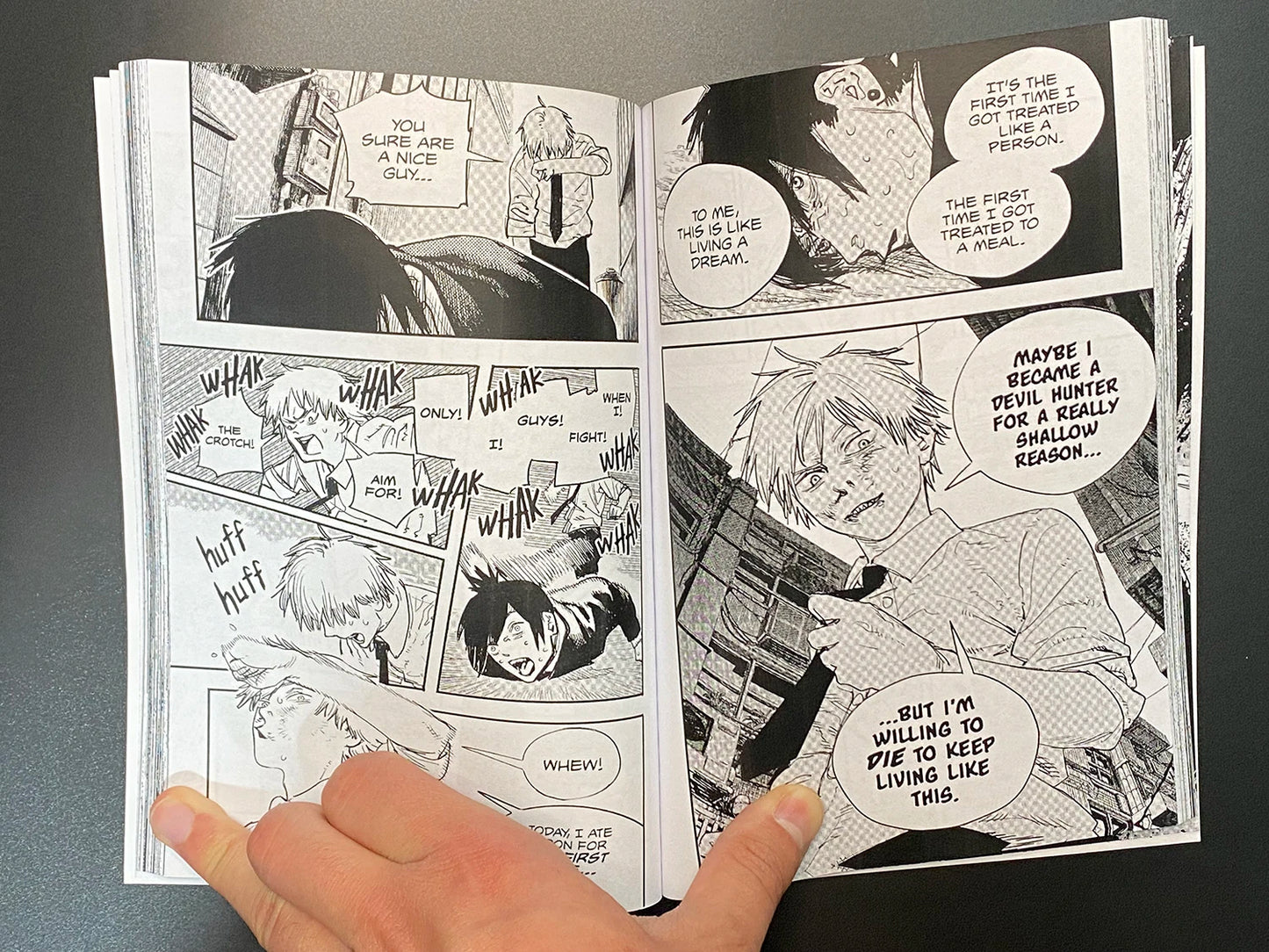 Open manga book with black and white illustrations and text bubbles, held by a hand.