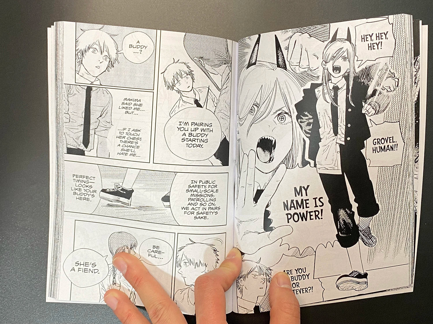 Open manga book with character illustrations and text bubbles on a dark surface