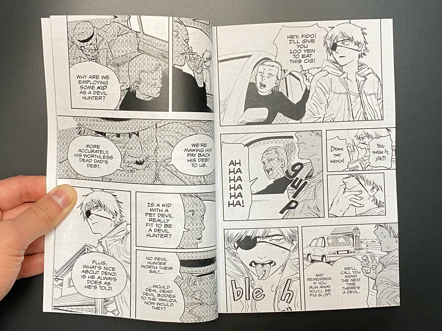 Open comic book with black and white illustrations held by a hand against a dark background