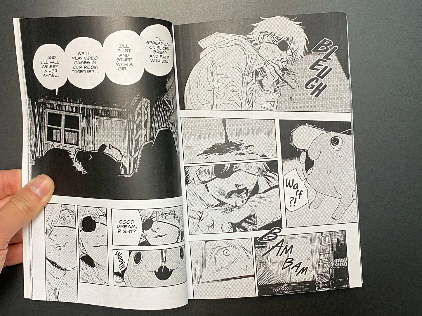 Comic book page with black and white illustrations held by a hand against a dark background