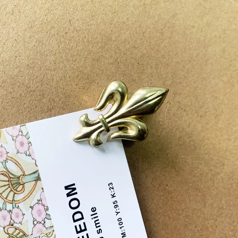 Gold fleur-de-lis decorative item on a card with floral design against a brown background