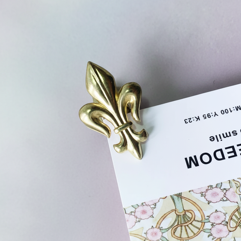 Gold fleur-de-lis clip on a floral-patterned card against a light purple background