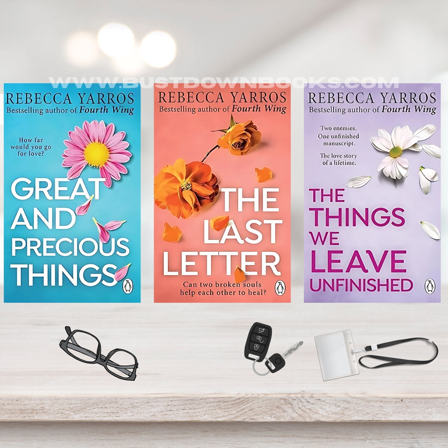 Three book covers by Rebecca Yarros on a shelf with glasses, keys, and a lanyard.