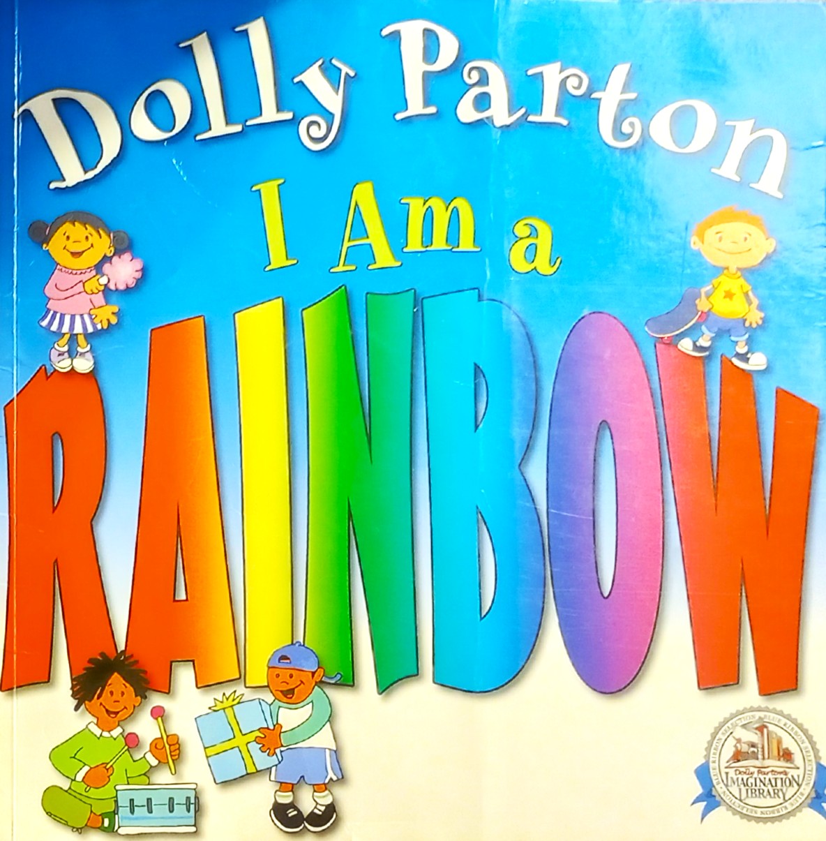 Children's book cover for 'I Am a Rainbow' by Dolly Parton, featuring large colorful rainbow letters on a blue-to-cream gradient background with cartoon children around the title.