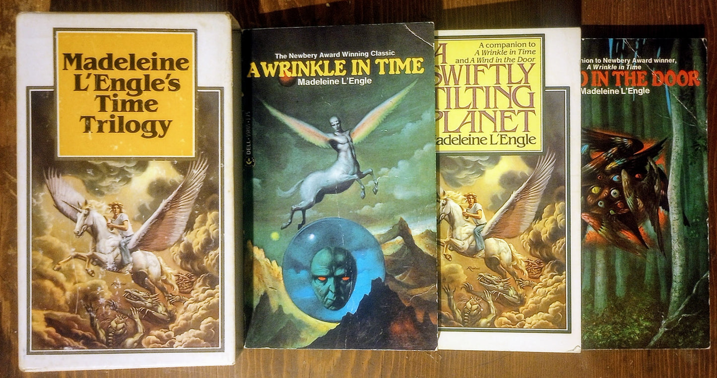 Three books from Madeleine L'Engle's 'Time Trilogy' next to the case cover art on a wooden surface.