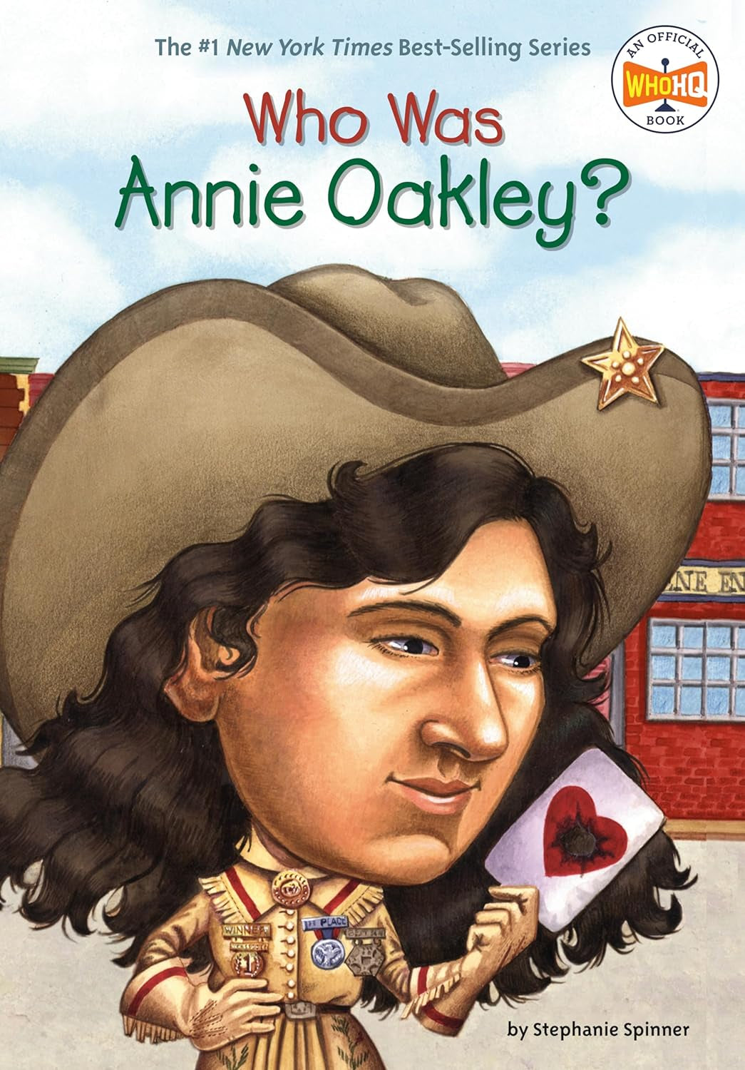 Cover of the children's book 'Who Was Annie Oakley?' featuring an illustration of a female figure wearing a cowboy hat and a white shirt, holding a toy gun and a red heart-shaped fan.