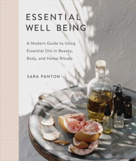 Book cover of 'Essential Well Being: A Modern Guide to Using Essential Oils in Beauty, Body, and Home Rituals' by Sara Panton with essential oils and fruit on a table.