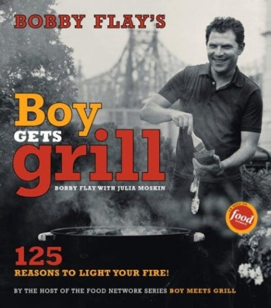 The cover of Bobby Flay's book 'Boy Gets Grill' featuring an image of Bobby Flay holding a grill, with a Manhattan skyline backdrop and text detailing the book's focus on grilling.