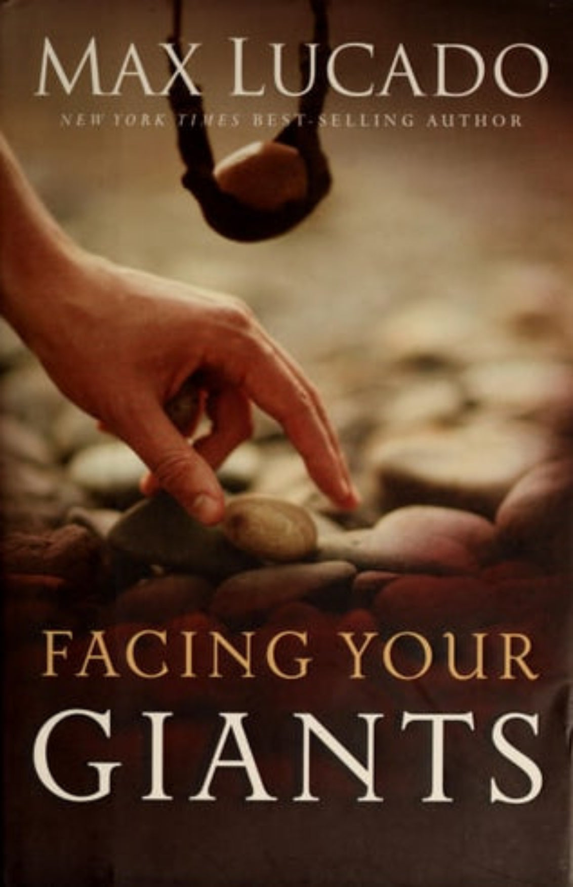 Book cover of 'Facing Your Giants' by Max Lucado with a hand reaching towards stones.