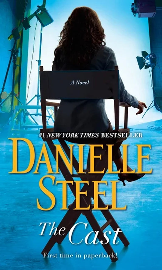 Book cover of 'The Cast: A Novel' by Danielle Steel, featuring a woman in a chair with a blue and yellow backdrop, indicating a scene likely from a television show or movie.