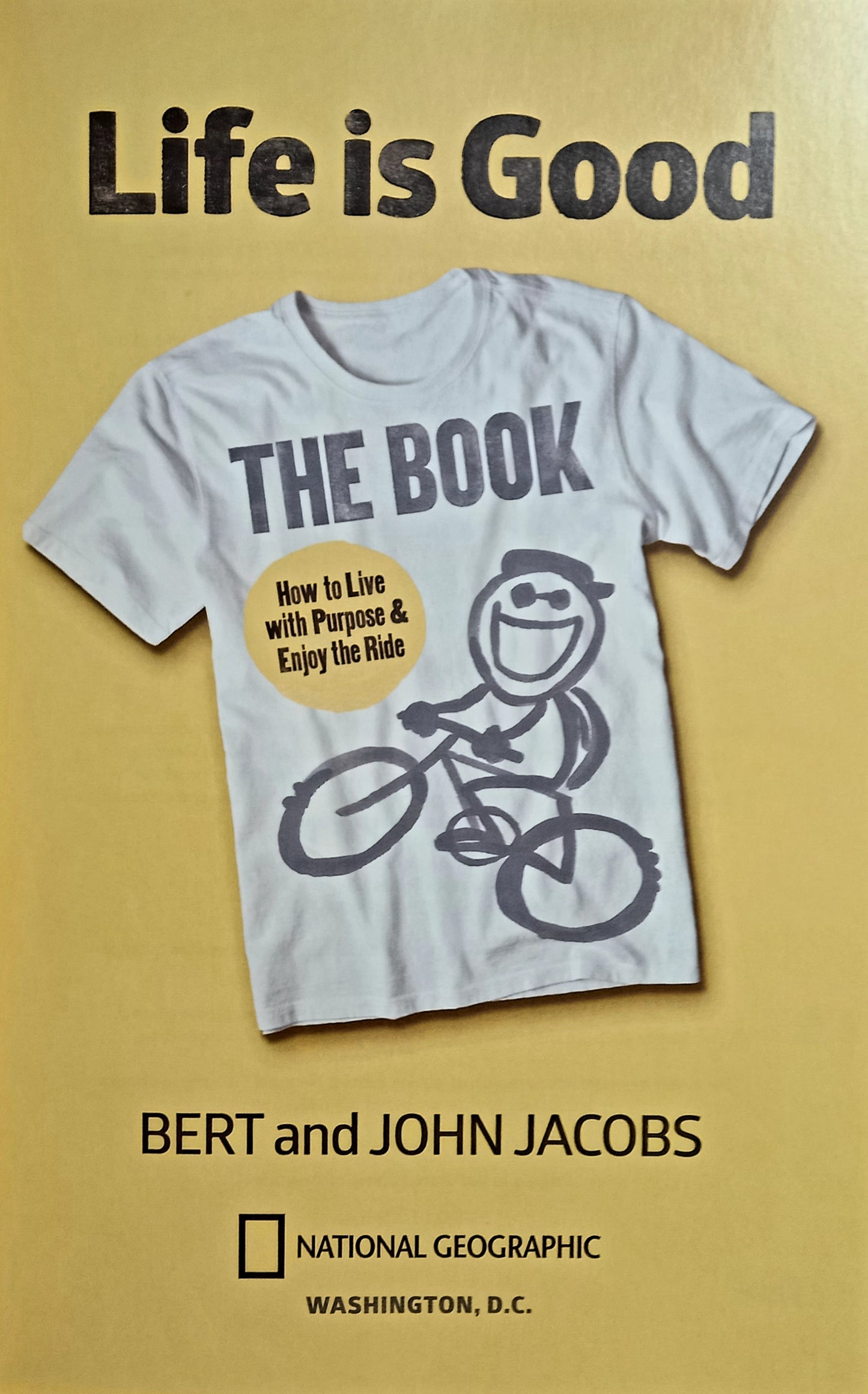 The cover of the book 'Life is Good: The Book' by Bert and John Jacobs, featuring a white t-shirt with the title and the brand's logo, against a yellow background.