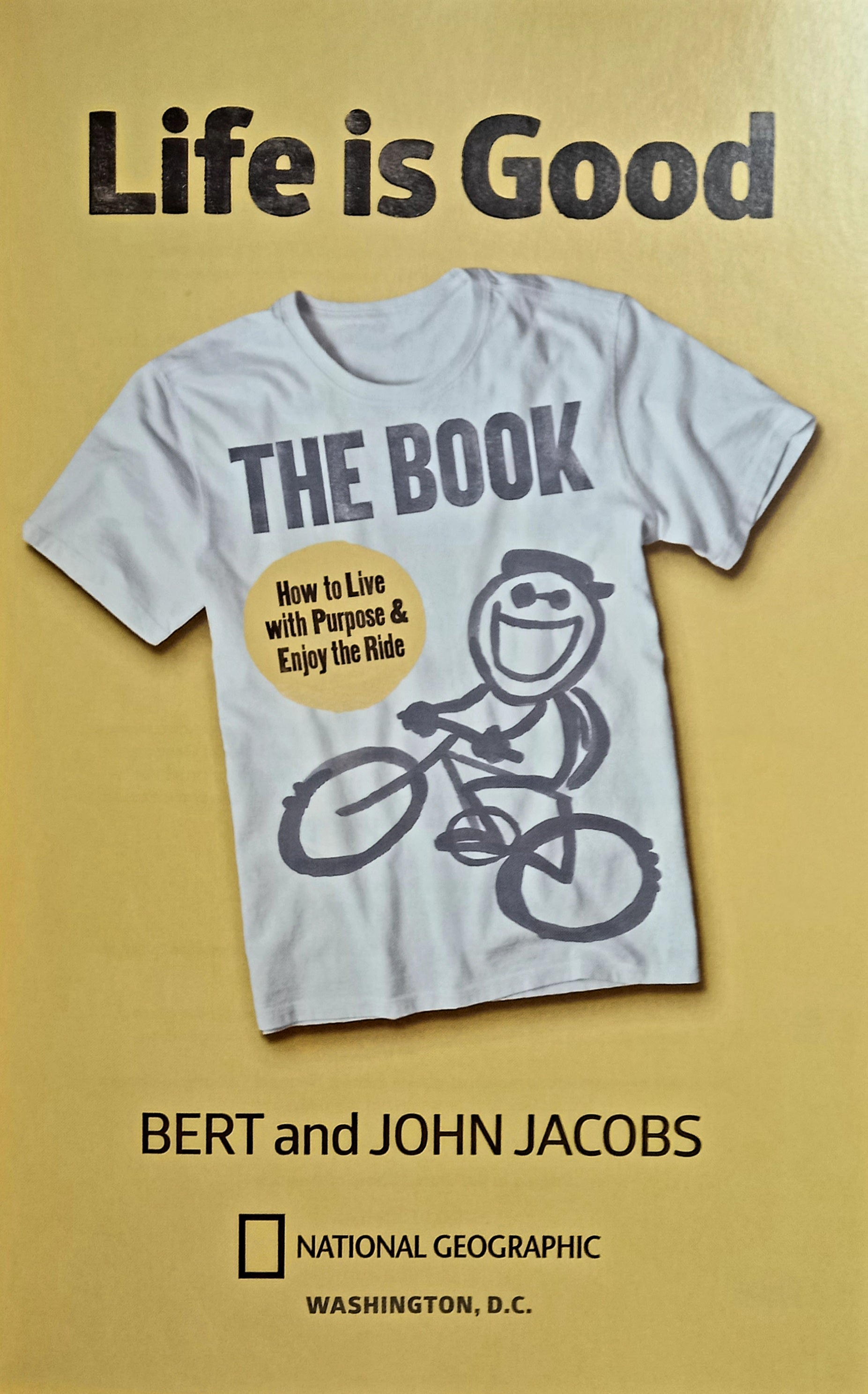 The cover of the book 'Life is Good: The Book' by Bert and John Jacobs, featuring a white t-shirt with the title and the brand's logo, against a yellow background.