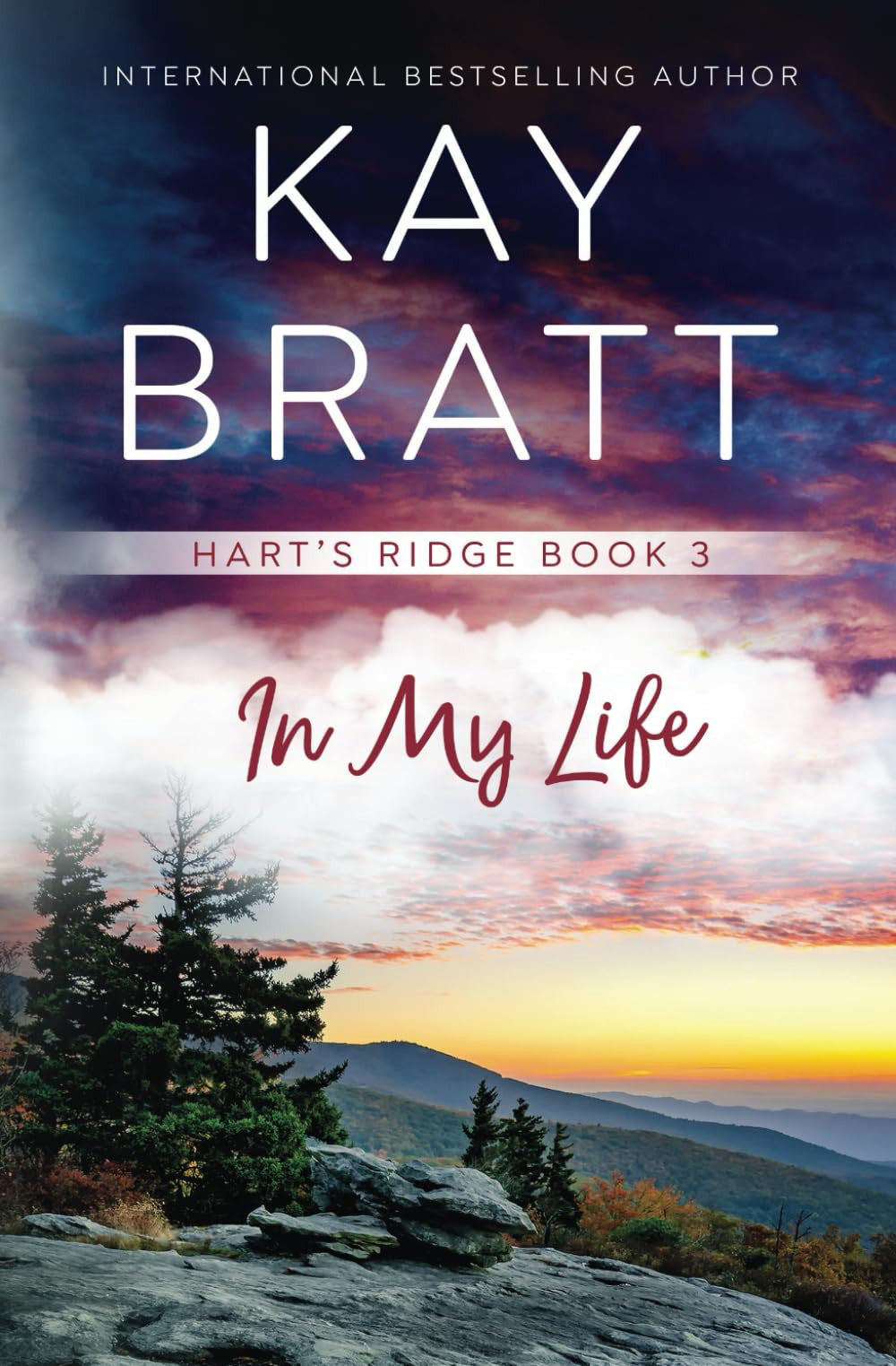 Book cover for 'In My Life' by Kay Bratt, featuring a mountain landscape at sunset with pine trees, clouds, and large white title text over a dramatic sky.