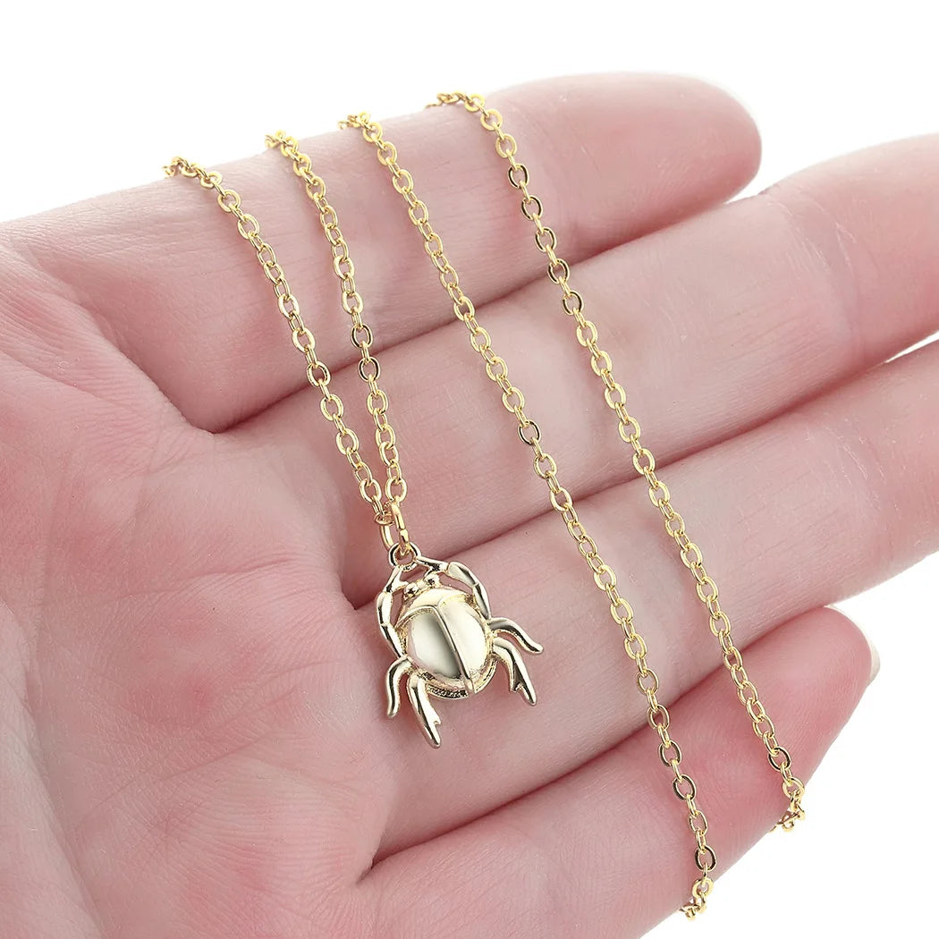 Gold necklace with a crab pendant held in a hand on a white background