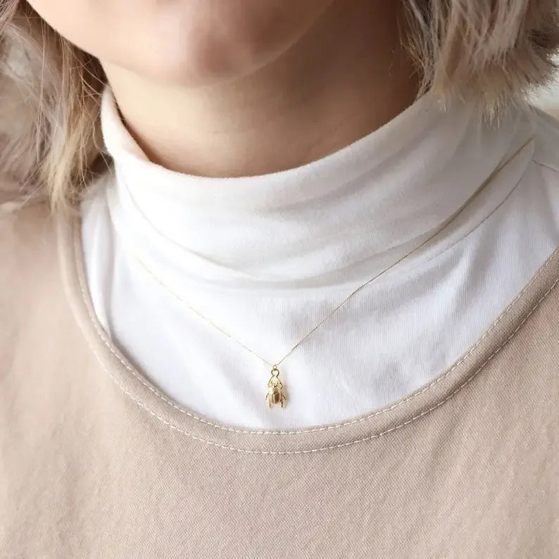 Gold necklace with a small pendant worn by a person in a white turtleneck and beige sweater.