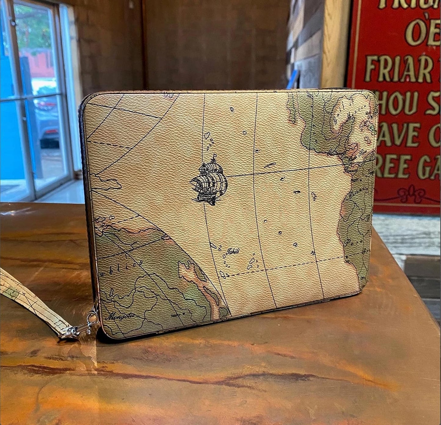 Atlas map themed leather case for travel ready backgammon set featured upright on a table with decorative wall art in room background.