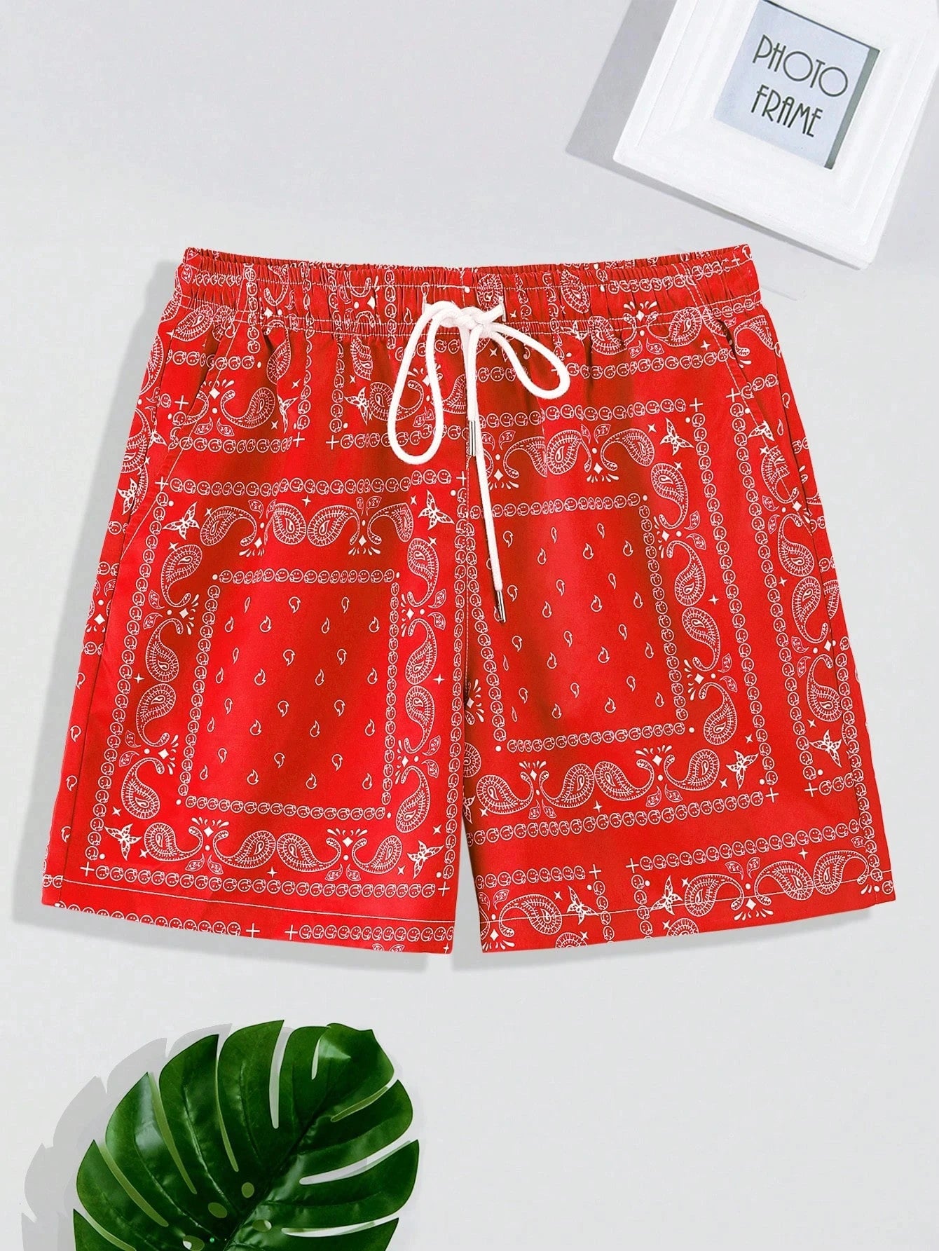 Red bandana pattern paisley shorts on a white background with a green leaf and photo frame.