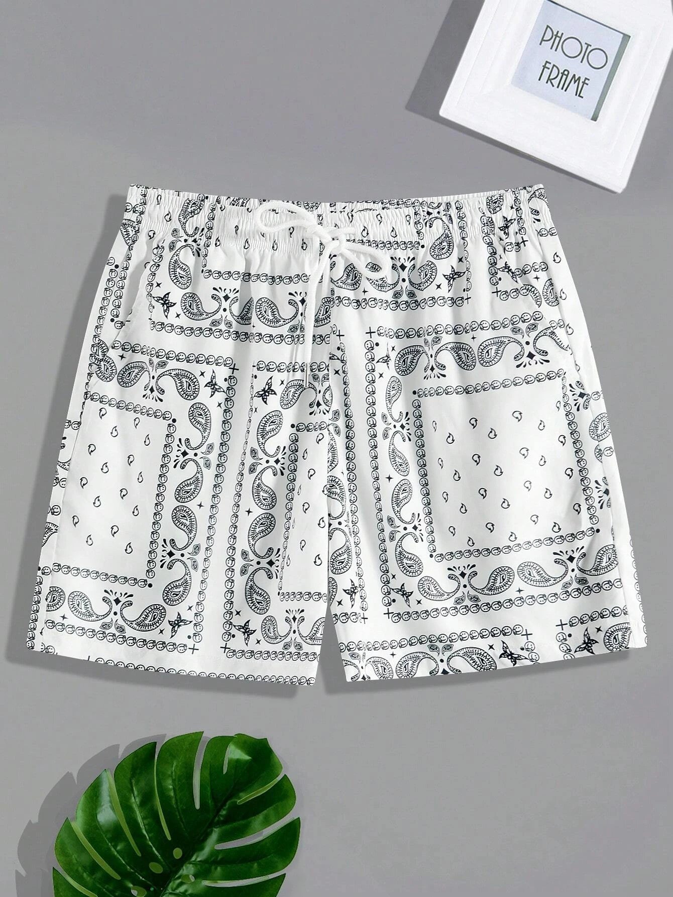 White & black paisley patterned bandana shorts on a gray background.