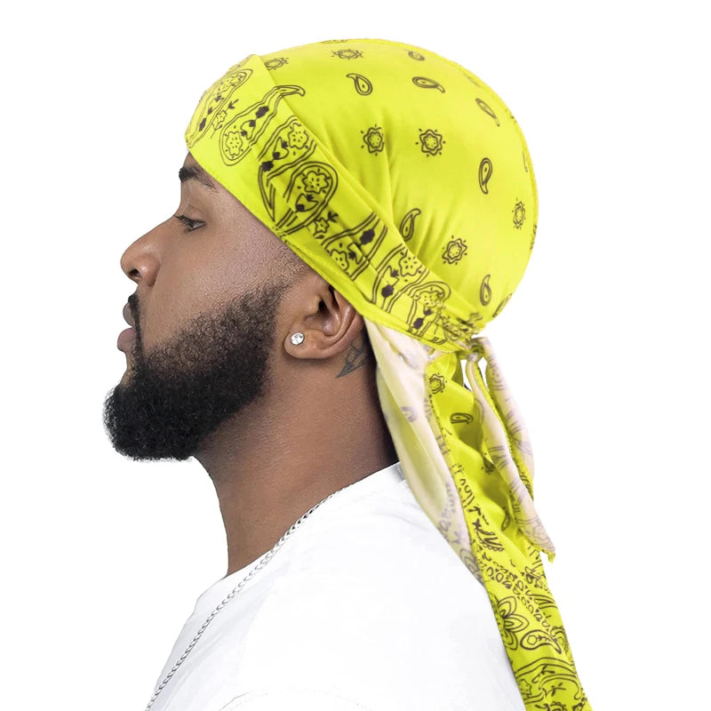 Man wearing a bright yellow bandana durag with black paisley patterns on a white background