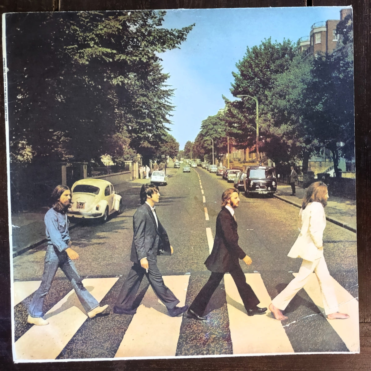 The Beatles' Abbey Road vinyl record album cover printed on a square product, photographed against a dark wooden background.