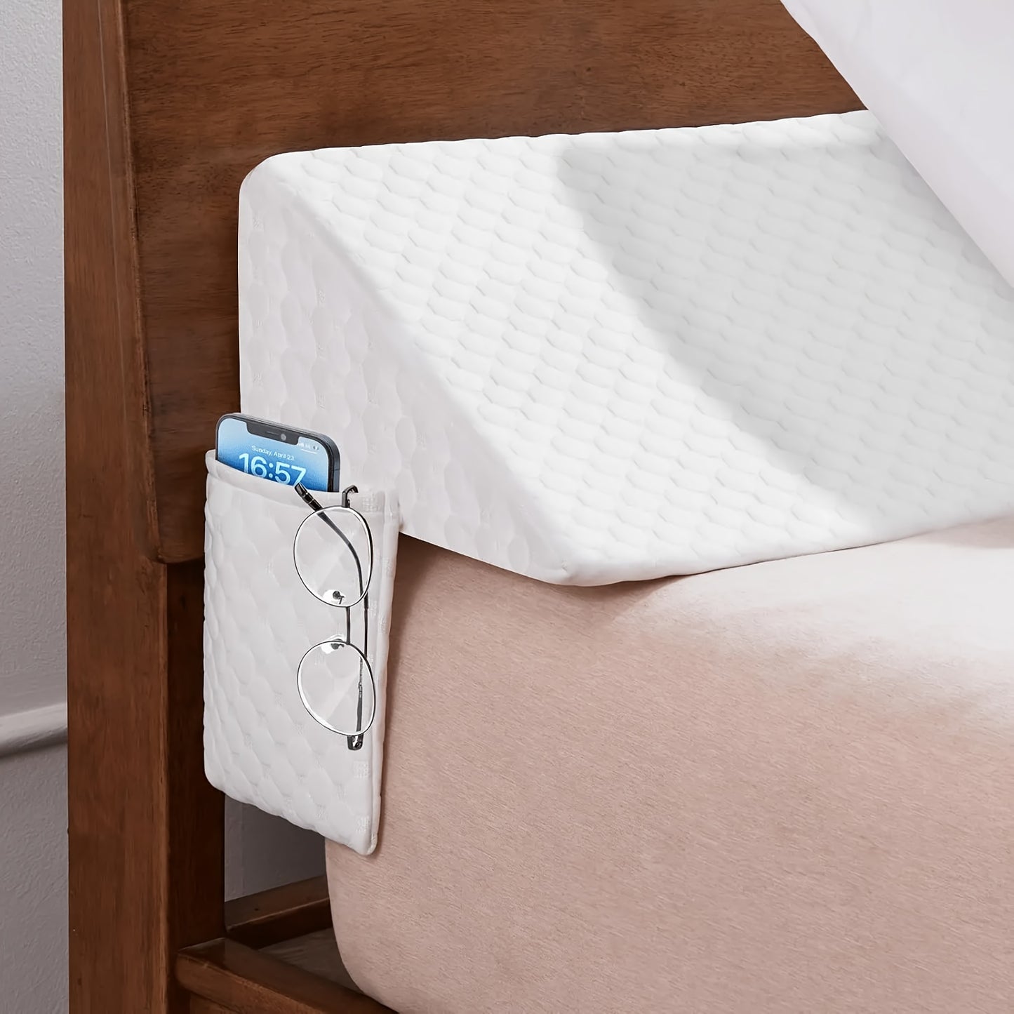 Bedside wedge pillow caddy attached to bed backboard headboard with a phone and glasses on it
