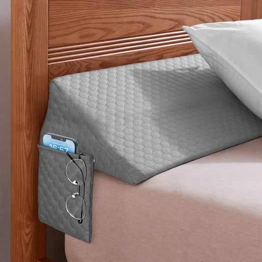 Grey wedge pillow on a bed with a wooden headboard and a smartphone in a pocket.