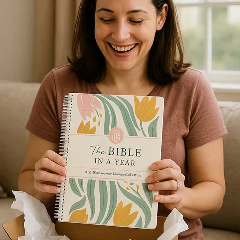 Woman holding a book titled 'The Bible in a Year: A 52 Week Journey Through God's Word' with floral design on cover