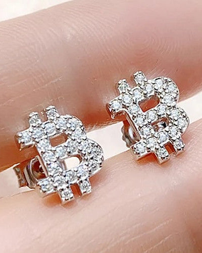 A pair of silver Bitcoin symbol stud earrings paved with clear cubic zirconia stones, shown resting on a person's fingers.