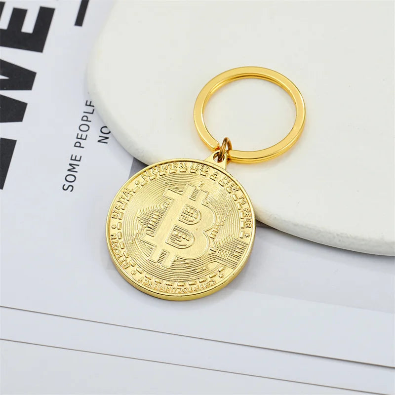 Gold Bitcoin keychain on a white surface with a magazine in the background