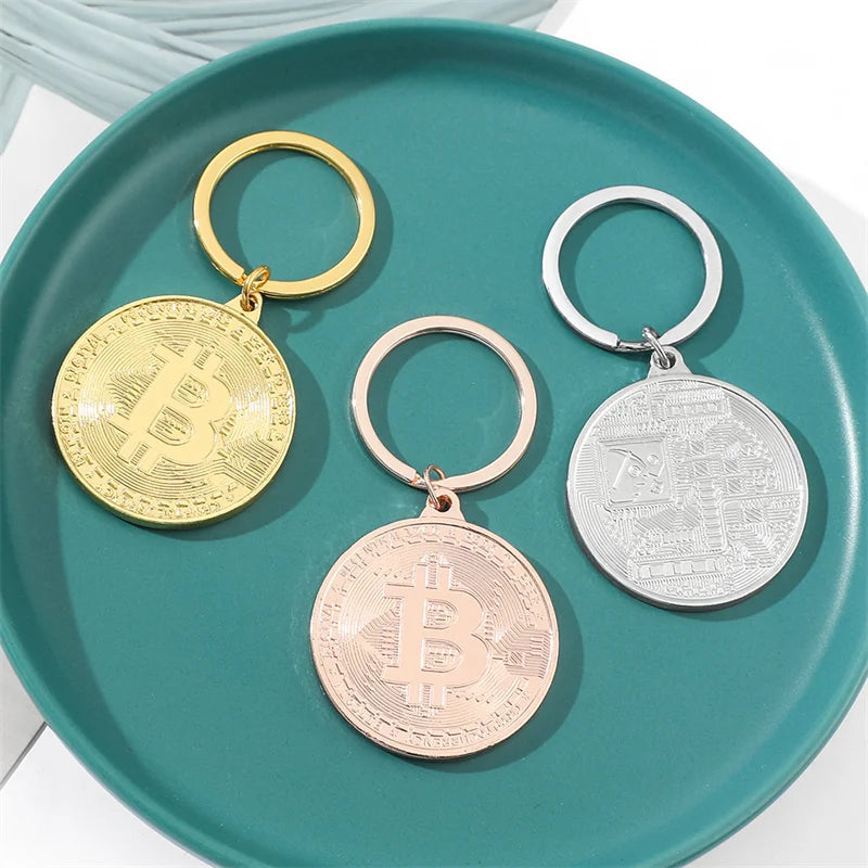 Three Bitcoin-themed keychains in gold, rose gold, and silver on a teal plate.