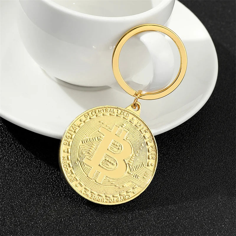 Gold Bitcoin keychain on a black surface with a white cup in the background
