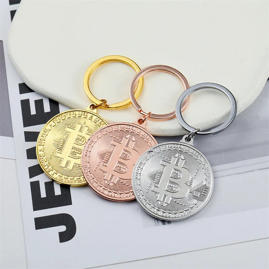 Three Bitcoin-themed keychains in gold, rose gold, and silver on a magazine page.