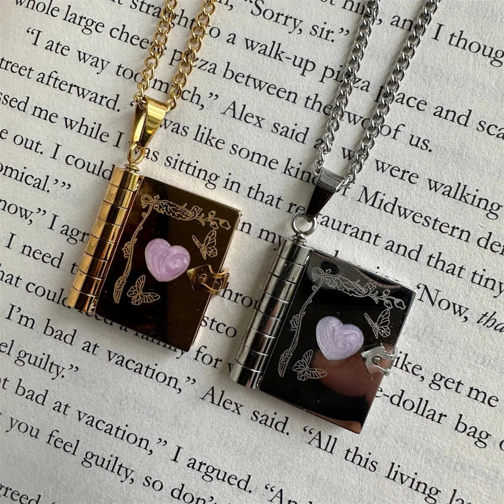 Two small book pendant necklaces with heart designs on a piece of paper with text from a novel.