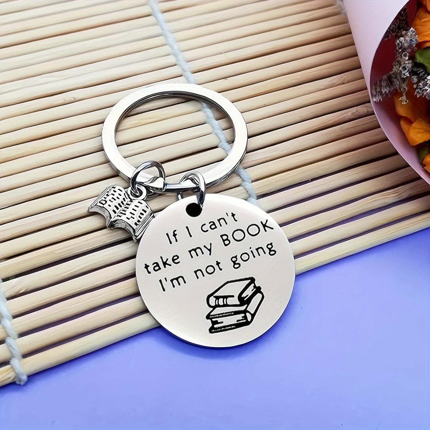 Keychain with 'If I can't take my BOOK, I'm not going' text on a wooden surface.