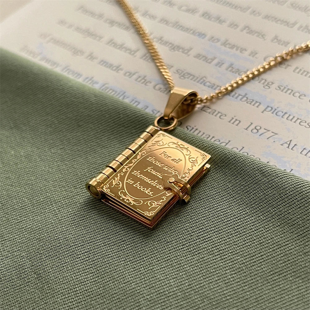 Gold book-shaped pendant necklace on a green fabric background