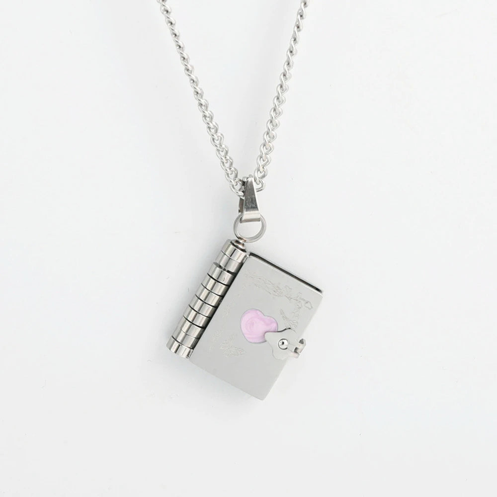 Silver book necklace with a rectangular pendant featuring a pink heart on the book front cover, over a white background.