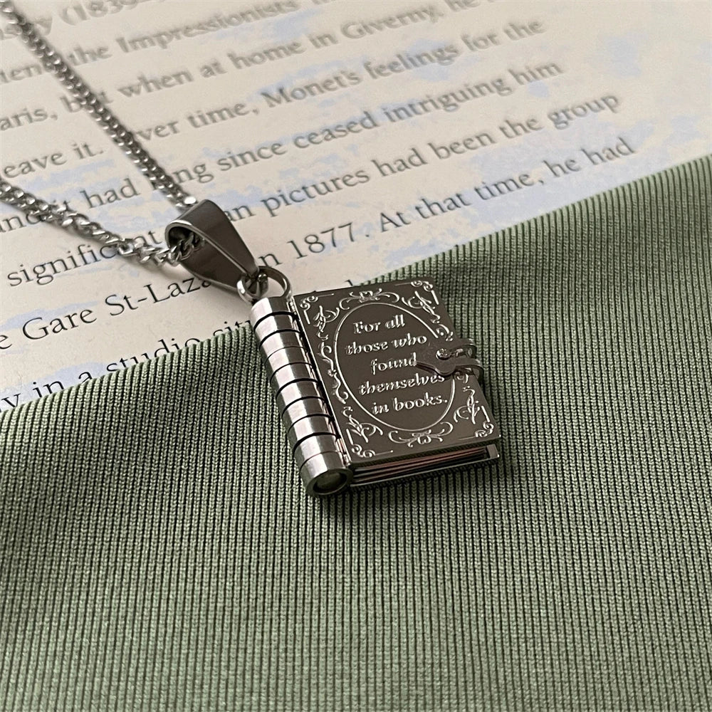 Silver book-shaped pendant with engraved text on a textured surface