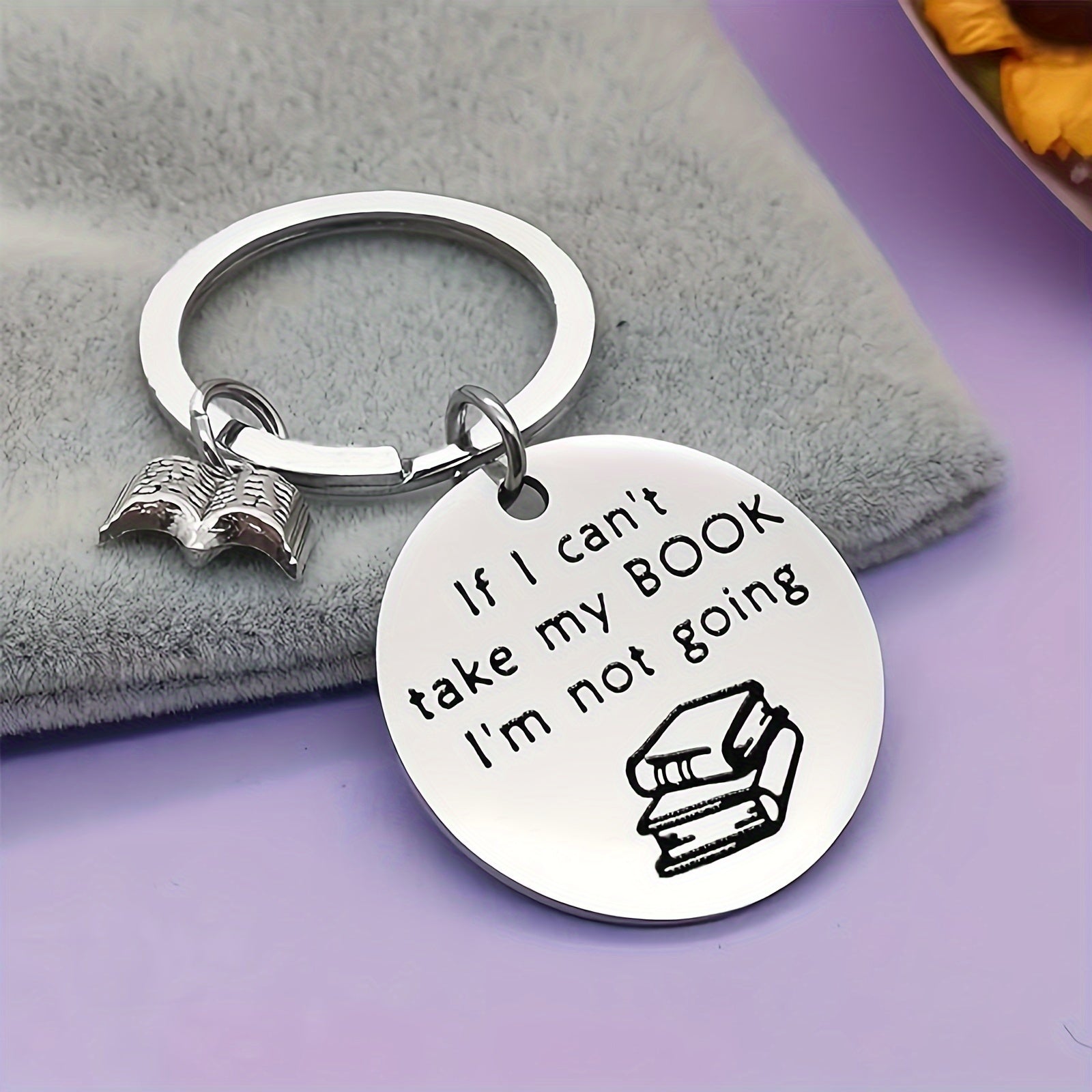 Silver keychain with book-themed design and humorous quote on a gray surface.