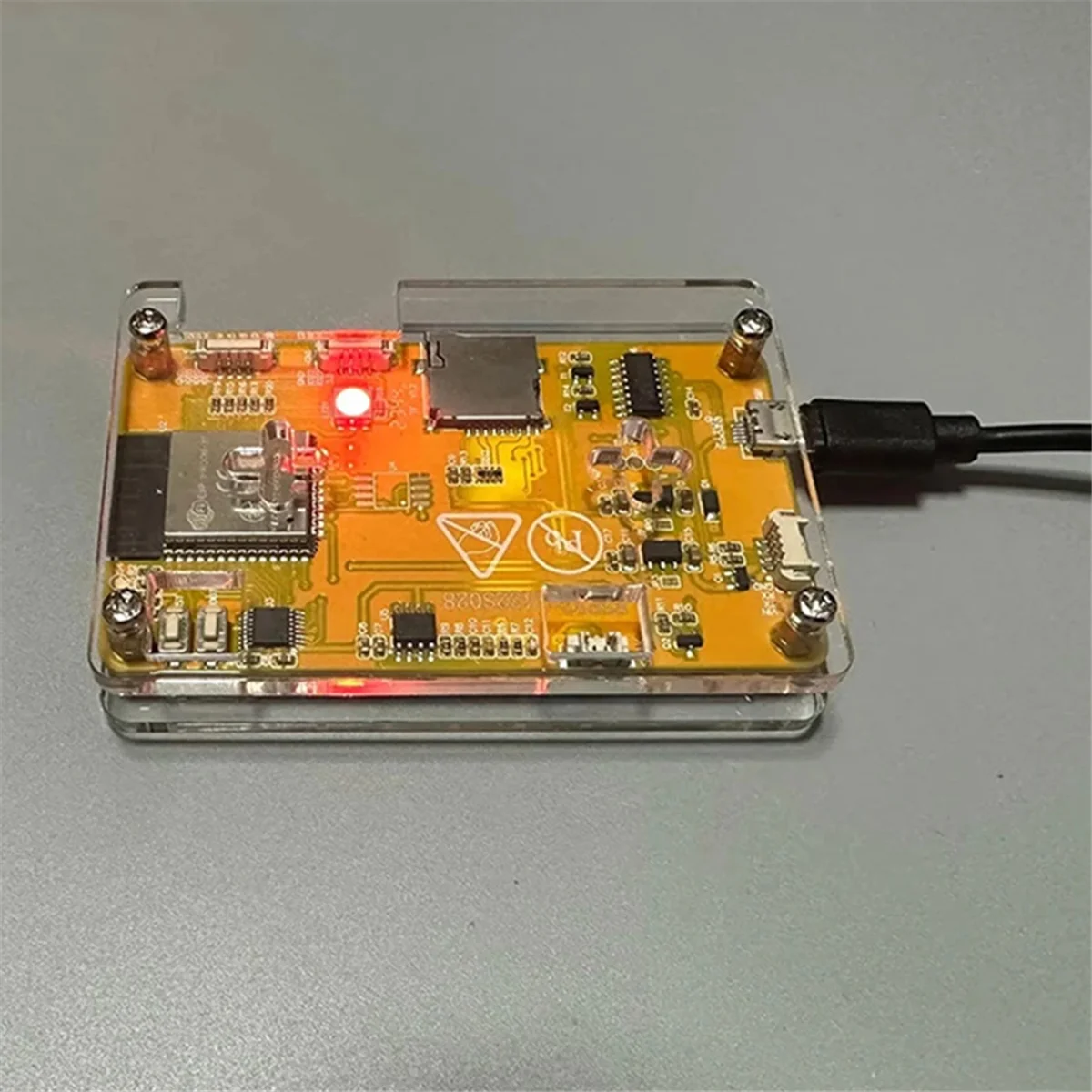 Electronic NerdMiner circuit board with components on a clear plastic base against a gray background