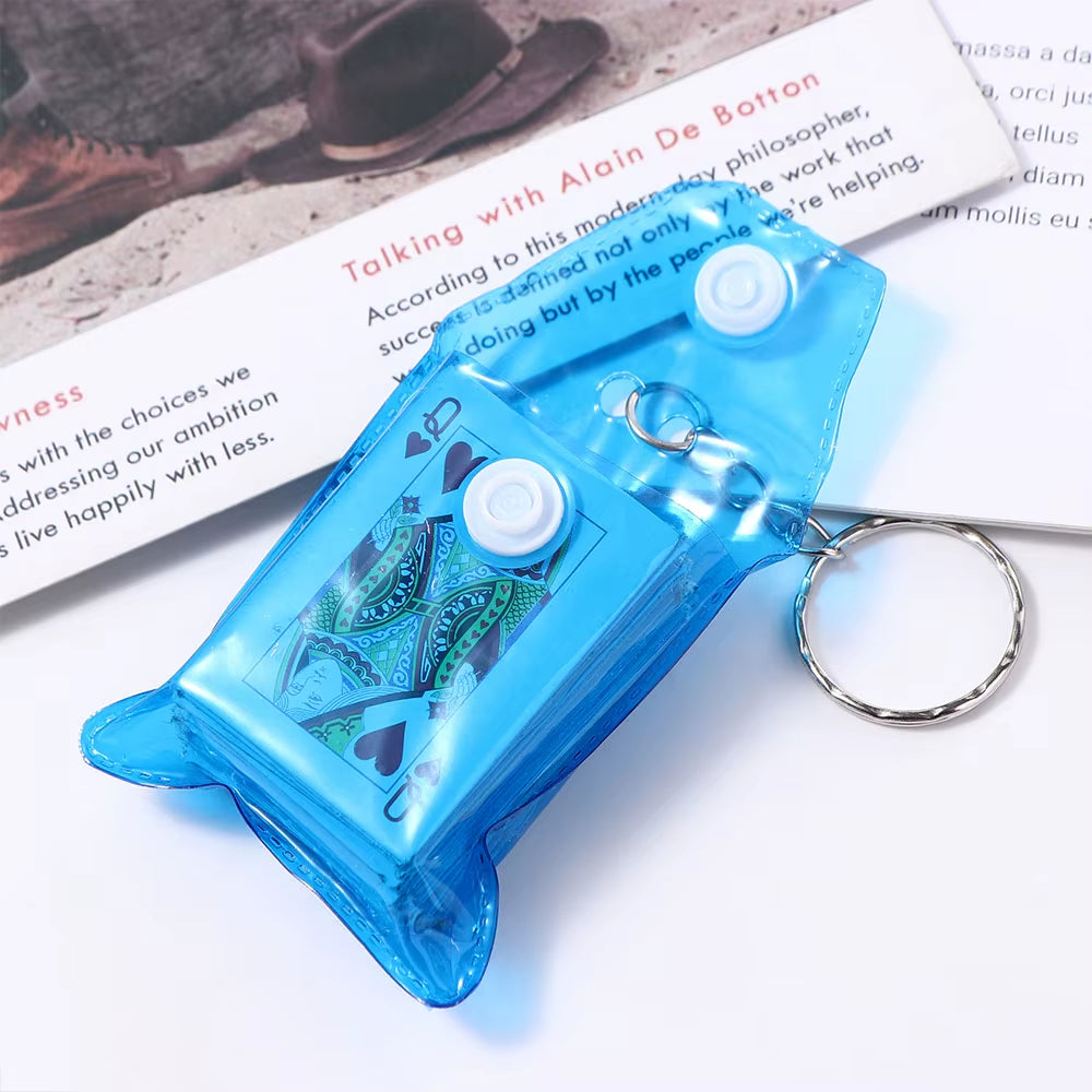 A mini playing card deck on a keychain, displayed on a desk next to a book.