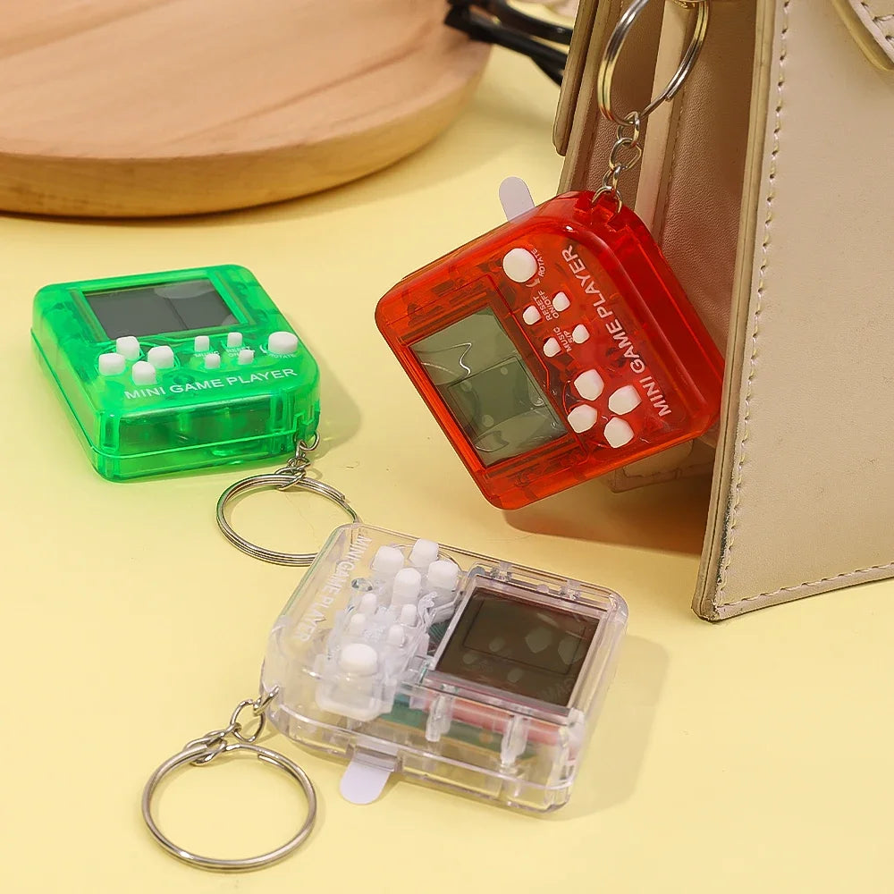 Three small electronic mini game keychains resembling vintage handheld games on a beige surface.
