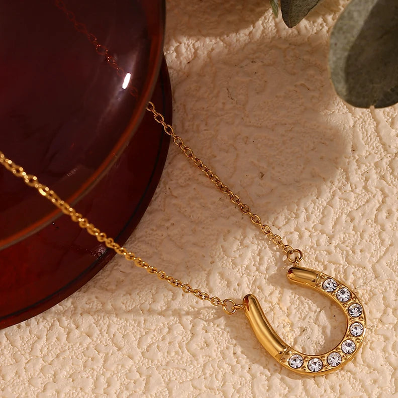 Gold horseshoe necklace with rhinestones on a textured beige surface