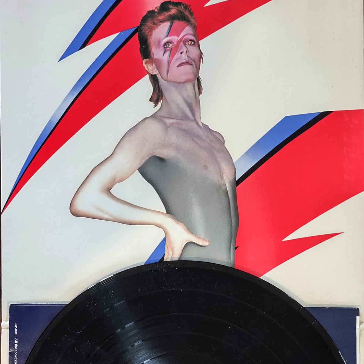 Image of Aladdin Sane by David Bowie vinyl LP case inner portrait illustration with wax record sat atop over included paper sleeve with song lyrics.